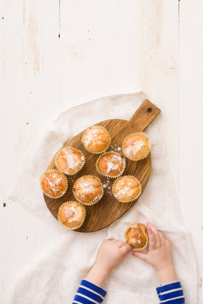 俯视图孩子的手与自制香草松饼。男孩拿着白木桌上的烤松饼。图片下载