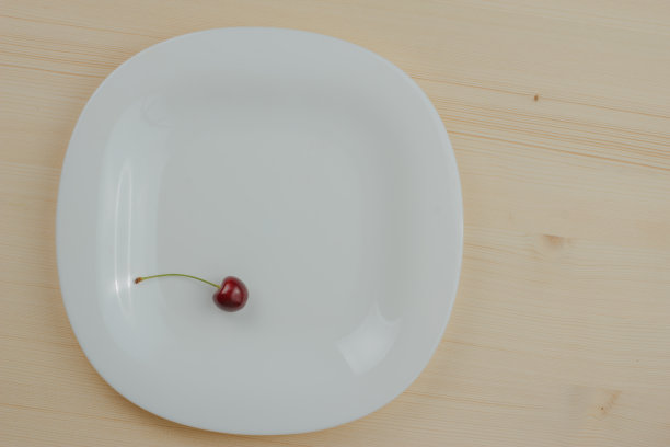 木桌上的白盘子里放着一颗樱桃。图片下载