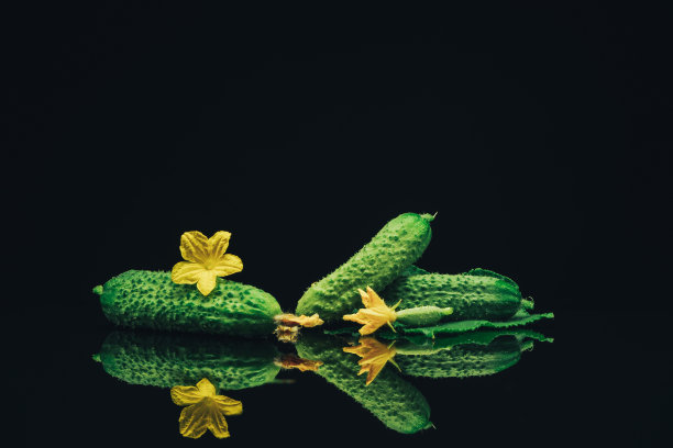 漂亮的新鲜黄瓜和黄色的花在黑色的玻璃桌子上，黑色的背景。图片下载