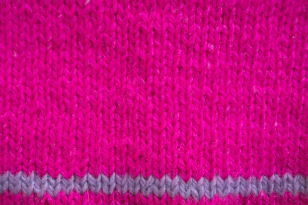 洋红色针织水平纹理冬季背景。一块亮粉色的碎片用紫色的带子系在一件儿童毛衣的针上。质地,俯视图图片下载