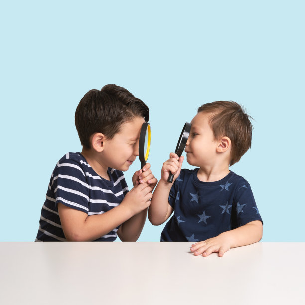 两个孩子在蓝色背景下玩放大镜图片下载