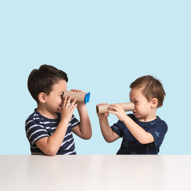 两个孩子在蓝色背景下玩纸望远镜图片下载