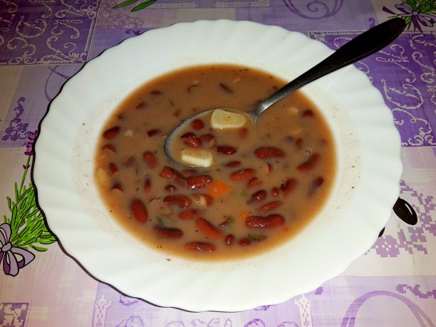 陶瓷盘子里放着豆荚汤，不锈钢勺子浸在里面，铺在紫色桌布上图片下载