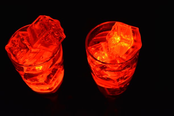 两杯不同寻常的香槟，一杯饮料和鲜红的冰片。在黑色的背景、令人印象深刻的照片和情人节的盛宴上，用塑料冰块照亮每个杯子里的饮料。图片下载