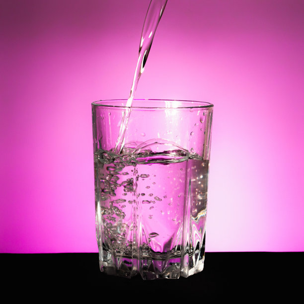 在紫色背景上的玻璃杯中泼水图片下载