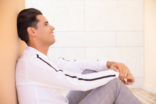 微笑的拉丁人坐在和躺在外面的墙上图片下载