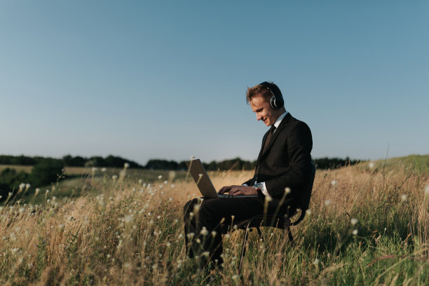 年轻快乐的商人带着耳机用视频聊天，在野外，坐在椅子上，侧面查看，户外图片下载