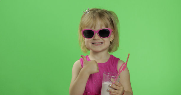 快乐的四岁孩子穿着粉红色的裙子和奶昔鸡尾酒。竖起大拇指图片下载
