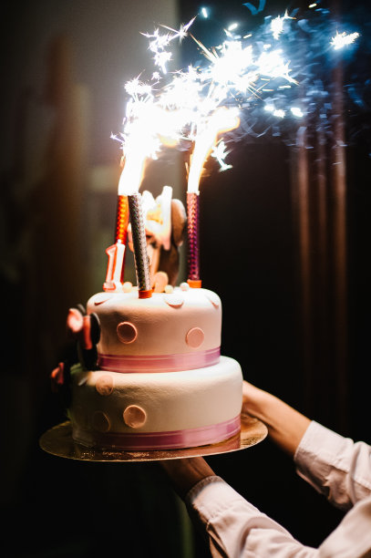 女人的手拿着一个带有烟花的节日蛋糕。
生日快乐。图片下载