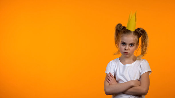 淘气的女学生在纸皇冠和双手交叉在胸前看凸轮图片下载
