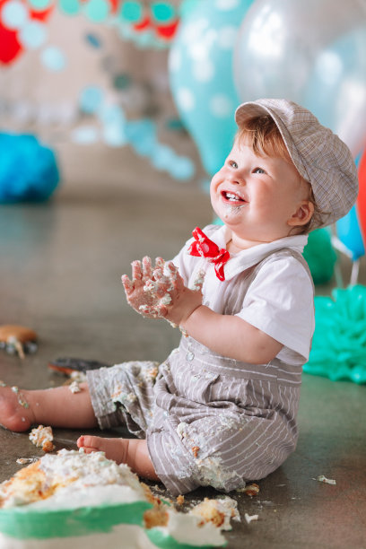 小男孩看一边与嘴巴覆盖在白色糖霜和蛋糕装饰工作室的背景。生日cakesmash聚会图片下载