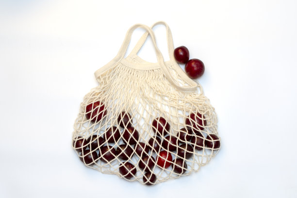 梅子在一个生态棉可重复使用的网袋，塑料袋的替代品，在白色的背景。前视图。图片下载