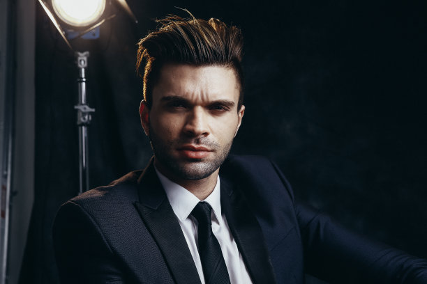 在黑色背景和电影灯光的工作室里坐着的英俊男人肖像图片下载