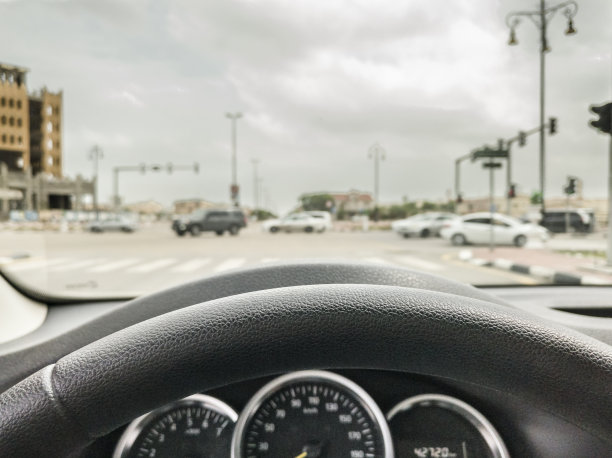 慢速行驶汽车的方向盘特写，背景是清晨现代城市高档区域的模糊景象图片下载