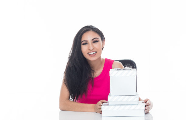 美丽的拉丁女性坐在一个白色的桌子上，拿着各种各样的礼品盒图片下载