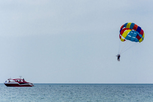 在蓝色的天空中，在平静的海洋上，一艘红色的摩托艇拖着一个人，用挽具悬挂在降落伞下面。在保加利亚黑海度假时，乘着降落伞在船后飞行图片下载
