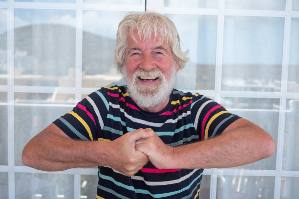 一个白胡子和头发的老人用手打手势。蓝色的眼睛和大大的微笑。有趣的表情。条纹t恤五彩缤纷图片下载