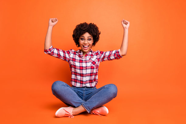 丰满的身体尺寸照片美丽的她她的黑皮肤女士坐地板腿交叉惊人的庆祝冠军穿眼镜休闲牛仔裤牛仔格子格子衬衫隔离明亮的橙色背景图片下载