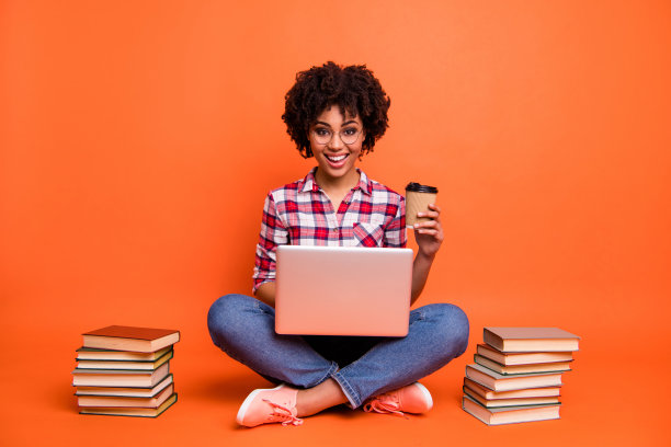 全身的照片卷曲的漂亮的女士坐地板手拉手笔记本外卖咖啡杯休息在线课程穿着眼镜休闲格子衬衫孤立的橙色背景图片下载