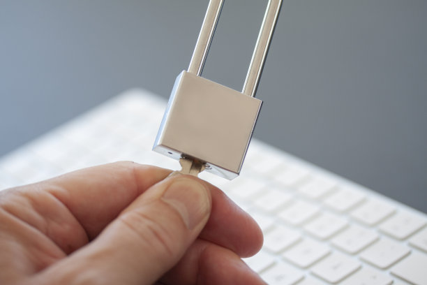 手指转动电脑键盘前的不锈钢挂锁上的钥匙。PC网络安全、数据安全及防病毒概念。——图片图片下载