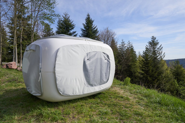 不寻常的现代帐篷，在户外休闲或睡眠的立方体形式，设置在山坡上的森林旁边的绿色草地上。睡帐篷图片下载