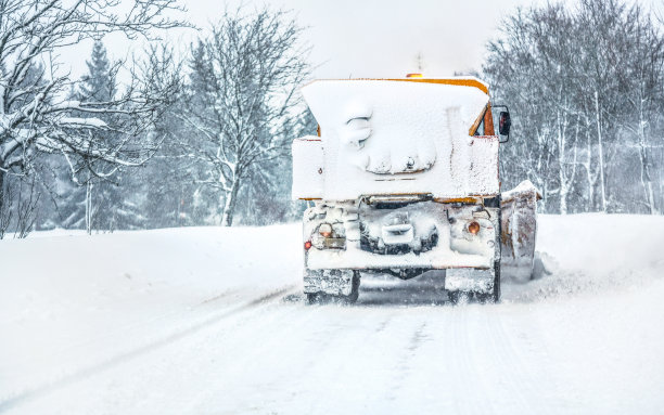 橙色公路养护砂砾犁卡车完全被积雪覆盖，清扫森林道路，从后面看汽车行驶图片下载