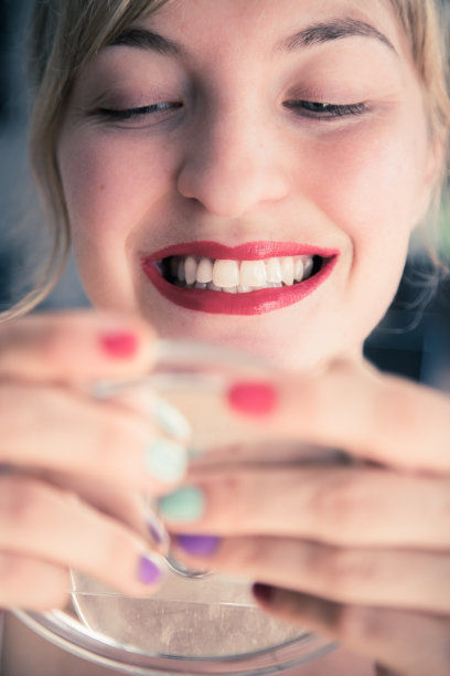 迷人的红唇:金发女郎涂着彩色指甲油看着镜子里的自己。从脸上切下来。图片下载