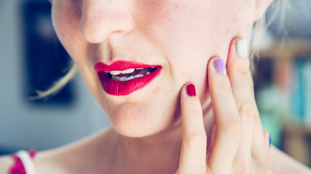 迷人的红唇:金发女郎涂着彩色指甲油看着镜子里的自己。从脸上切下来。图片下载