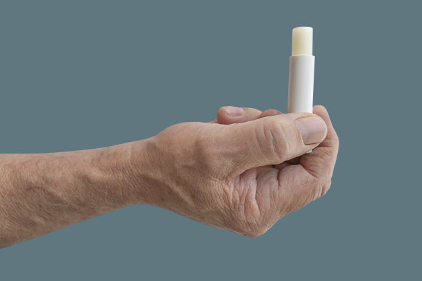 用男士的手在绿色柔和的背景上单独涂润唇膏图片下载