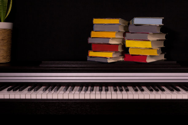 黑色背景的钢琴上有一堆彩色的书。图片下载
