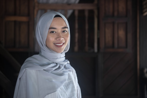 在传统的马来房屋前，马来西亚穆斯林妇女戴着头巾的肖像图片下载