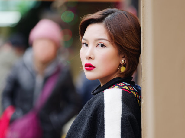 美丽的年轻女子在黑色大衣看着镜头与人群街道的背景。户外时尚写真魅力中国时尚淑女。情感、人、美、生活理念。图片下载