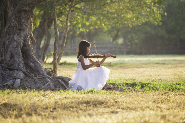 一个穿着白色裙子的亚洲女孩正在拉小提琴图片下载