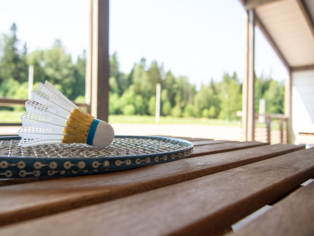 乡村别墅阳台上的木制乡村家具。两把羽毛球拍和毽子放在木桌上。背景中郁郁葱葱的绿叶变得模糊了。图片下载