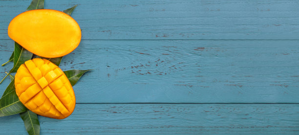 新鲜的芒果-美丽的切碎的水果，绿色的叶子在深蓝的木材背景。热带水果设计理念。平的。前视图。本空间图片下载