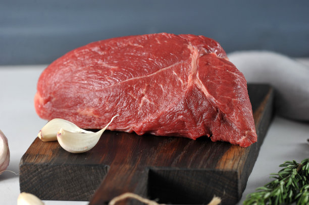 生牛肉放在深色木板上。肉旁边放着两瓣大蒜。图片下载