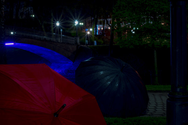夜景公园雨后灯火通明的桥和点亮黑色和红色的伞。曝光不足的照片。图片下载