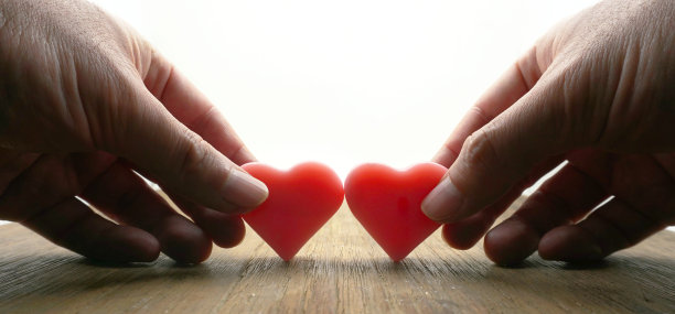 一对恋人捧着粉红色的心，放在木桌上。图片下载