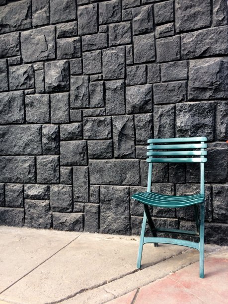 黑色石墙或栅栏背景上的绿色椅子图片下载