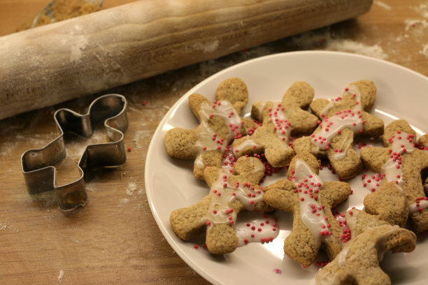 这是在厨房里用木制擀面棍和铬制姜饼人饼干切割机制作的新鲜姜饼人食谱，自制/家庭烘焙的圣诞饼干和装饰有白色糖霜/粉色糖屑的饼干图片下载