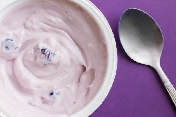 蓝莓酸奶在塑料杯上的紫色背景与金属勺子-俯视图特写照片的酸奶在塑料锅图片下载