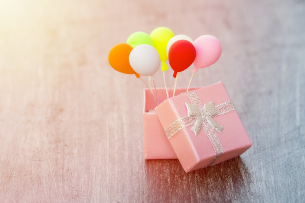 木制背景上的银色丝带和彩色气球的粉色礼盒。最小hollyday概念图片下载