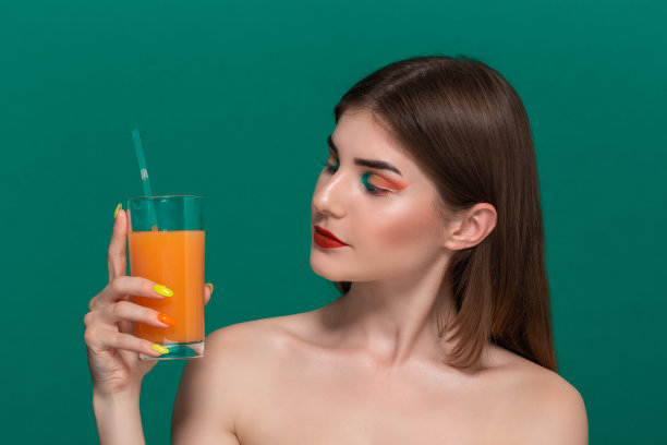 漂亮的年轻女子的特写肖像与明亮的颜色化妆捧着橙汁近脸图片下载