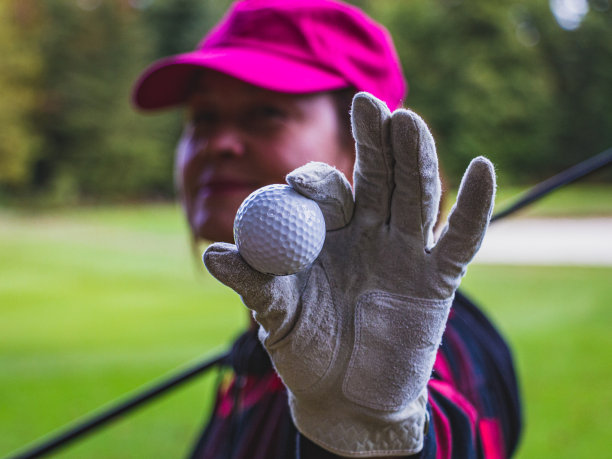 高尔夫球游戏。白色纹理皮革高尔夫手套和高尔夫球近距离，选择性聚焦，模糊的背景。图片下载