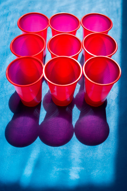 一次性塑料杯。在红色的杯子上，明亮的太阳照耀着，形成了一个阴影。回收和处理塑料。自然采光图片下载