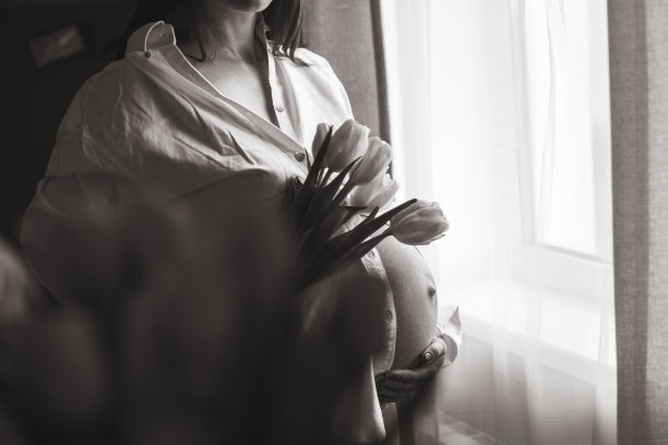 怀孕的女人手捧鲜花，站在窗边，黑白照片图片下载