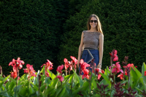 快乐的年轻女子站在公园附近的鲜花，偷拍的户外肖像美丽的黑发图片下载
