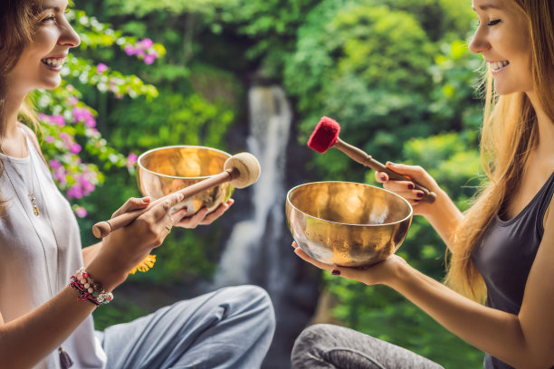 温泉沙龙的尼泊尔佛铜歌唱碗。年轻漂亮的女人做按摩治疗唱歌碗在温泉对着瀑布。健全的治疗，娱乐，冥想，健康的生活方式和身体护理理念图片下载