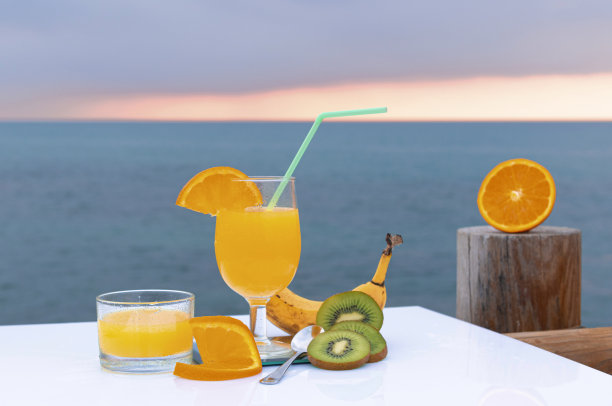 香蕉，绿猕猴桃片，橙子片，一片橙子和新鲜橙汁在一个玻璃杯-美味的水果为主的饮食-在大海的背景地平线图片下载