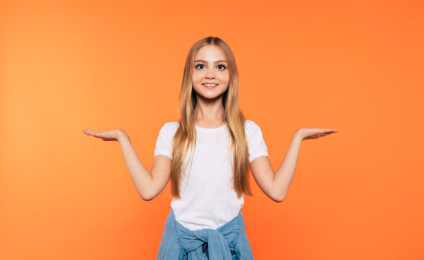 美丽的小金发女孩是指和显示在工作室的黄色墙壁上孤立的白色t恤的东西图片下载